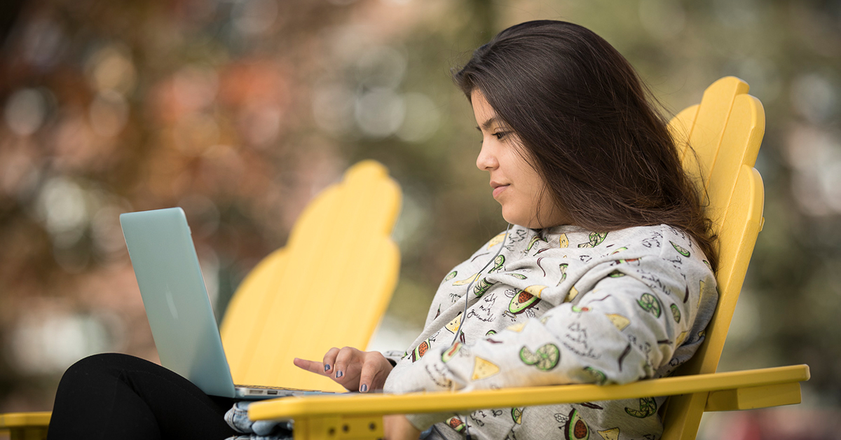 Student sitting outdoors on campus with a laptop